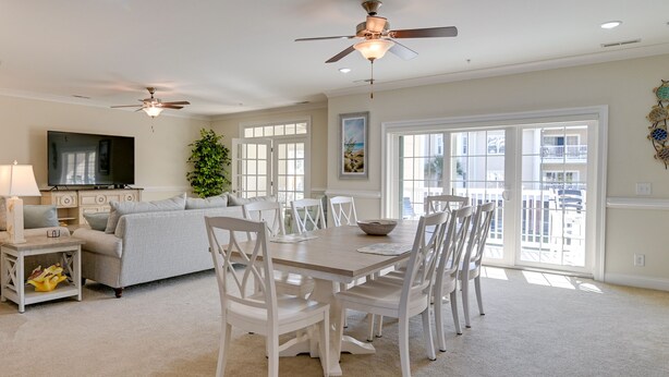 A spacious living room with a dining area, a ceiling fan, a flat-screen TV, and large windows. - Murrells Inlet Golf Resort Condo: 1 Mile to Beach! (Murrells Inlet)