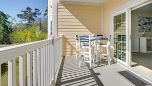 A balcony with a white railing, a table with blue chairs, and a view of trees and a building. - Murrells Inlet Golf Resort Condo: 1 Mile to Beach! (Murrells Inlet)