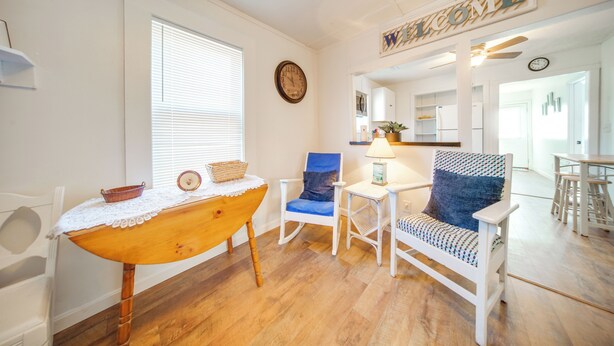 A room with a wooden table, a blue chair, a white chair, and a small table with a lamp. - Charming Cottage w/ Yard < 1 Mi to Lake Erie! (Geneva)