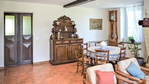 Een eetruimte met een ronde tafel, stoelen, een houten kast en een grote klok.
