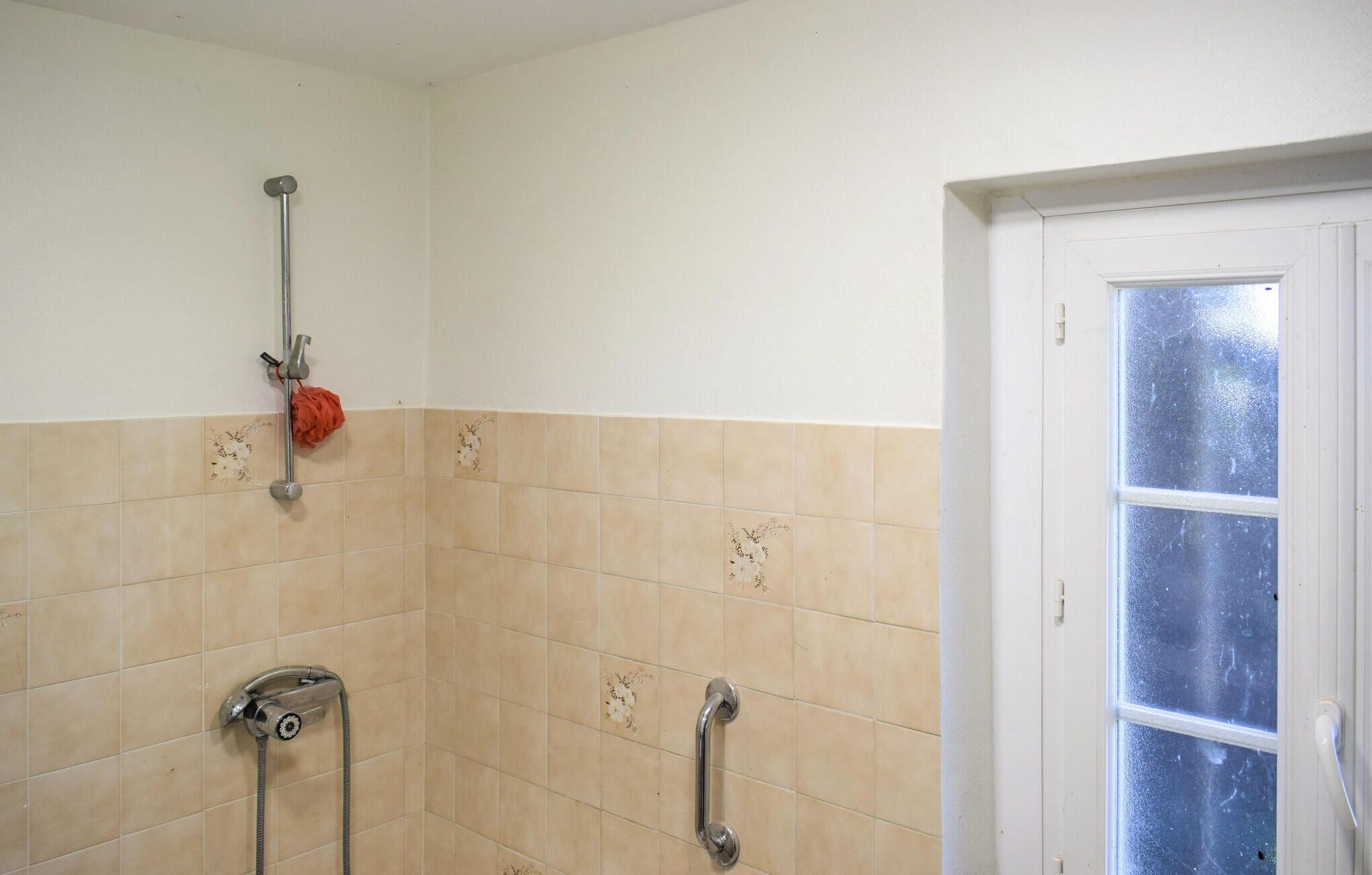 Un baño con azulejos color beige, una ducha con cabezal de ducha manual y una puerta blanca con ventanal esmerilado.