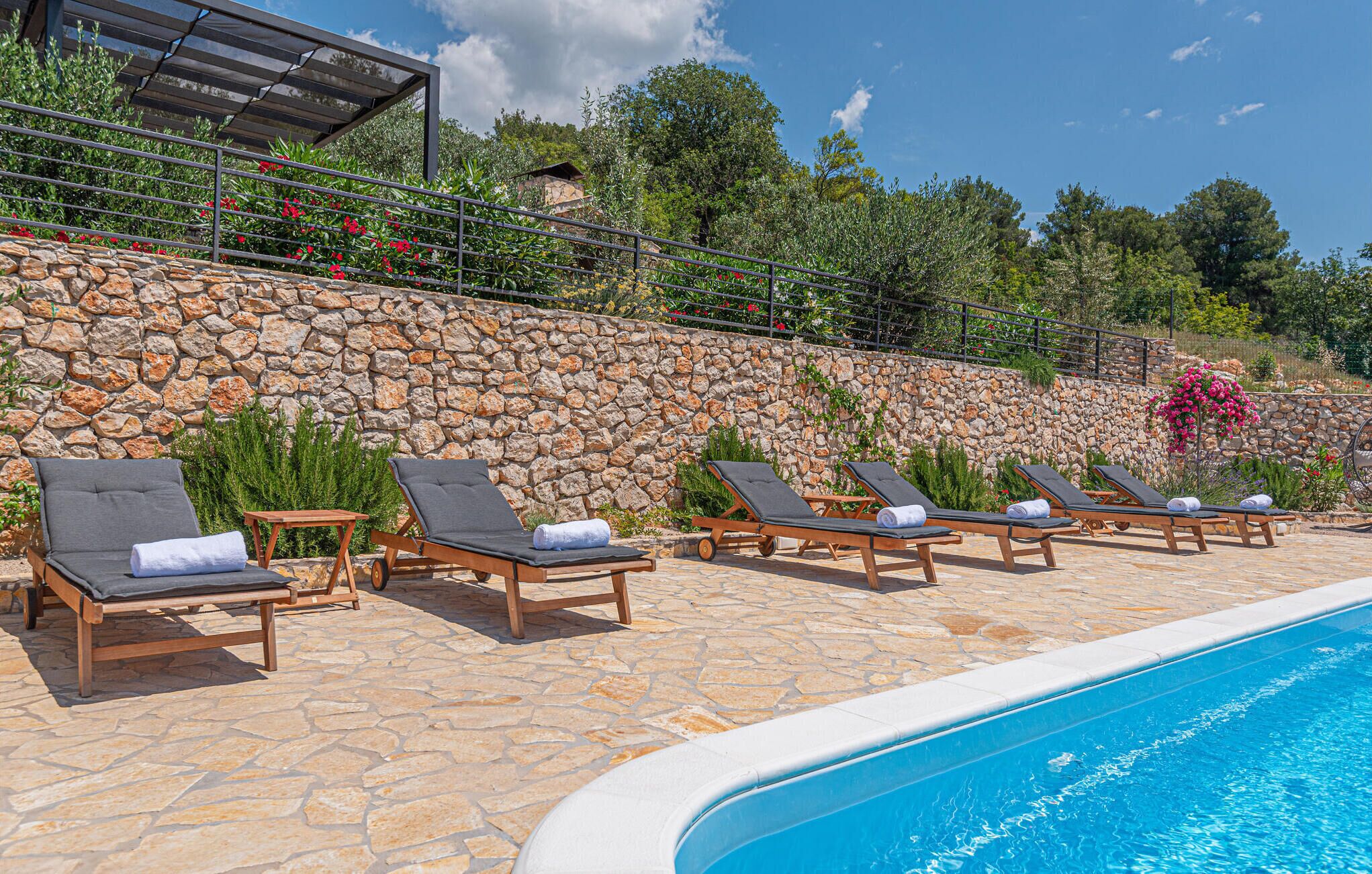 A poolside area with sun loungers, a stone wall, and a clear blue sky.