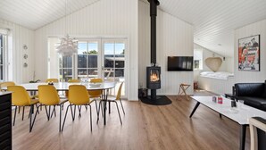 Ein modernes Wohnzimmer mit hohen Decken, einem Kamin, einem Essbereich mit gelben Stühlen und einem an der Wand befestigten Fernseher.