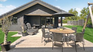 Ein modernes Haus mit einer Terrasse, Gartenmöbeln und einem großen Sonnenschirm.