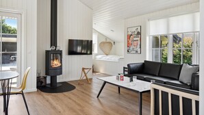 Ein modernes Wohnzimmer mit Kaminofen, einer schwarzen Ledersofa, einem Esstisch und einem großen Fenster mit Blick auf Grünflächen.