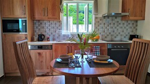 A modern kitchen with wooden cabinets, a Bosch dishwasher, and a window offering a view of greenery. - La Trouvaille Holiday Chalets (Mahé Island)