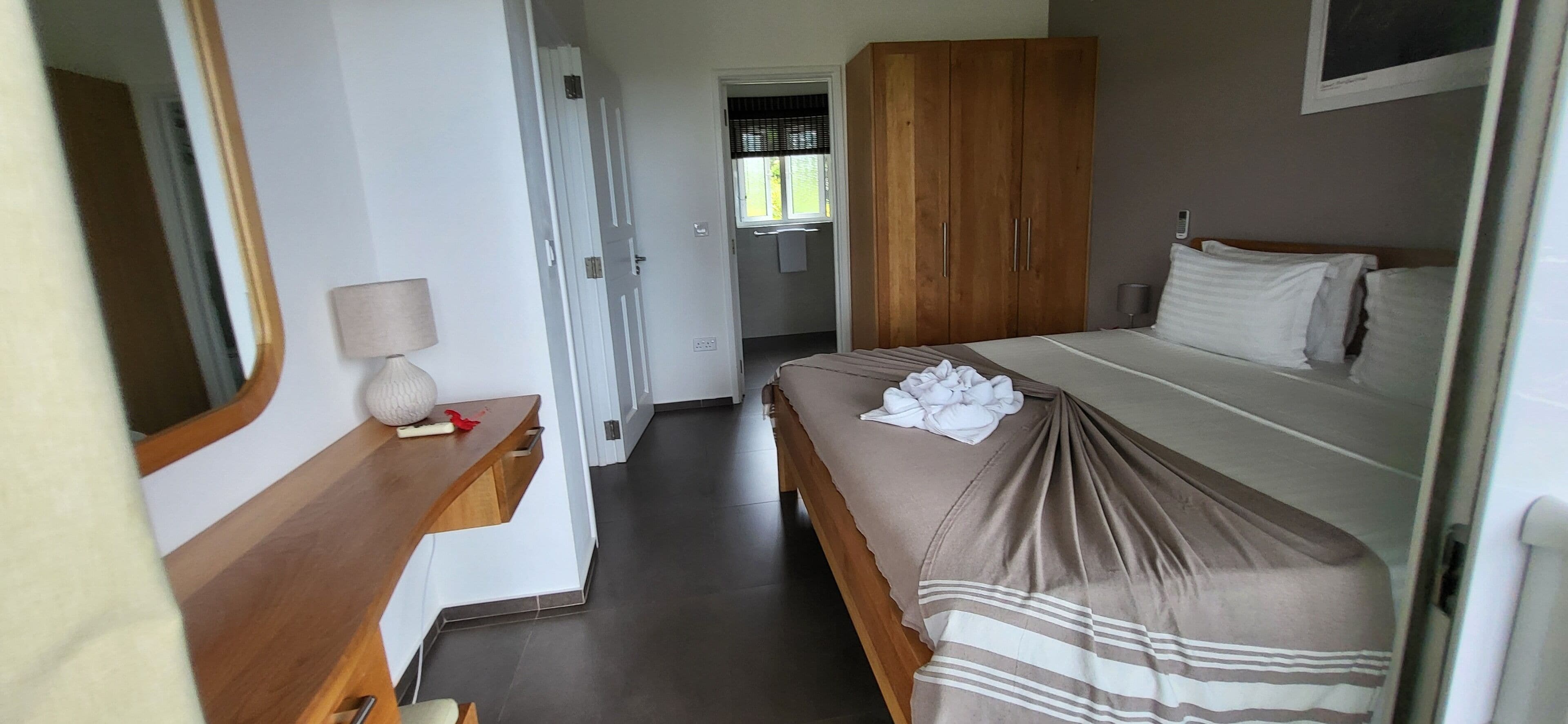 A bedroom with a bed, a wooden wardrobe, a bedside table with a lamp, and a mirror.