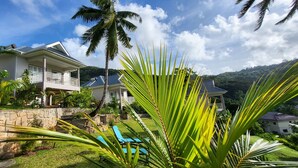 A two-story house with a balcony, surrounded by lush greenery and palm trees. - La Trouvaille Holiday Chalets (Mahé Island)