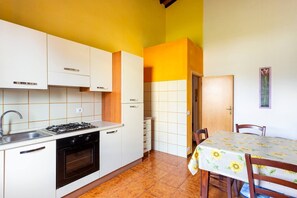 A compact kitchen with white cabinets, a gas stove, and a sink. There is a dining area with a table covered by a sunflower tablecloth and two chairs.