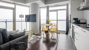 Un appartement moderne doté d’un balcon, d’un coin repas avec une table ronde et des chaises, d’une cuisine équipée d’une machine à café et d’un téléviseur à écran plat fixé au mur.