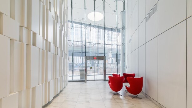Un hall d’entrée moderne avec une façade vitrée, des murs blancs et des chaises rouges.