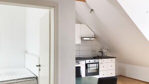 Een kleine keuken met een fornuis, oven en koffiezetapparaat, en een apart slaapgedeelte met een bed.