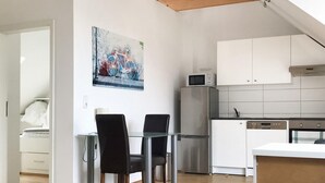 Een moderne keuken met witte kasten, een roestvrijstalen koelkast en een magnetron. Er is een eethoek met een glazen tafel en zwarte stoelen.