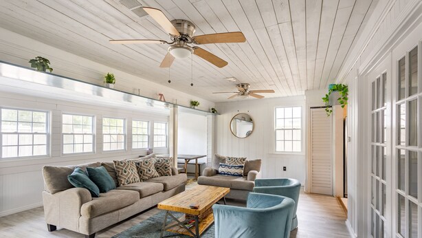 Ein geräumiges Wohnzimmer mit einem beigefarbenen Sofa, blauen Sesseln, einem Holztisch und einem Deckenventilator.