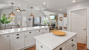 A spacious kitchen with white cabinetry, a large island, pendant lighting, and a ceiling fan. - Luxury Beach Home with Gas Fireplace, Fast WiFi, BBQ & Outdoor Seating (San Diego)