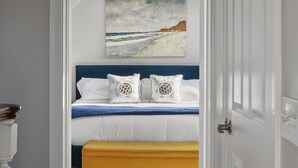 A bedroom with a bed, pillows, a bedside table, and a painting of a beach scene. - Luxury Beach Home with Gas Fireplace, Fast WiFi, BBQ & Outdoor Seating (San Diego)