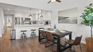 A modern kitchen with white cabinets, stainless steel appliances, and a dining area with a wooden table and bar stools. - Luxury Beach Home with Gas Fireplace, Fast WiFi, BBQ & Outdoor Seating (San Diego)