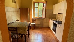A kitchen with a dining area, a window with shutters, and a tiled floor. - Maison Antoinette - Lavender (Toscana)