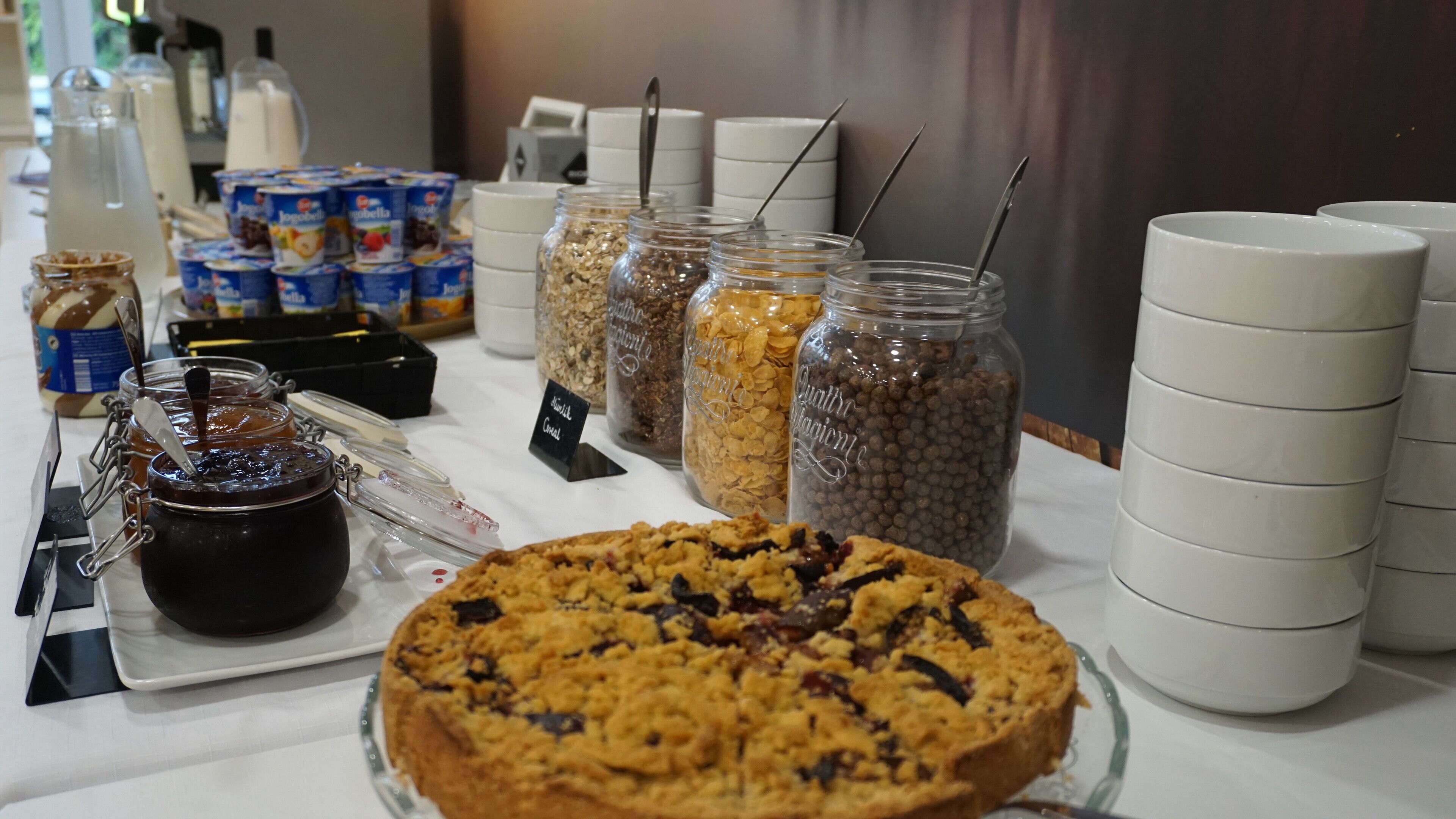 Una mesa de buffet con diferentes alimentos, incluyendo botes de granola, cereales y una tarta de galletas grande.