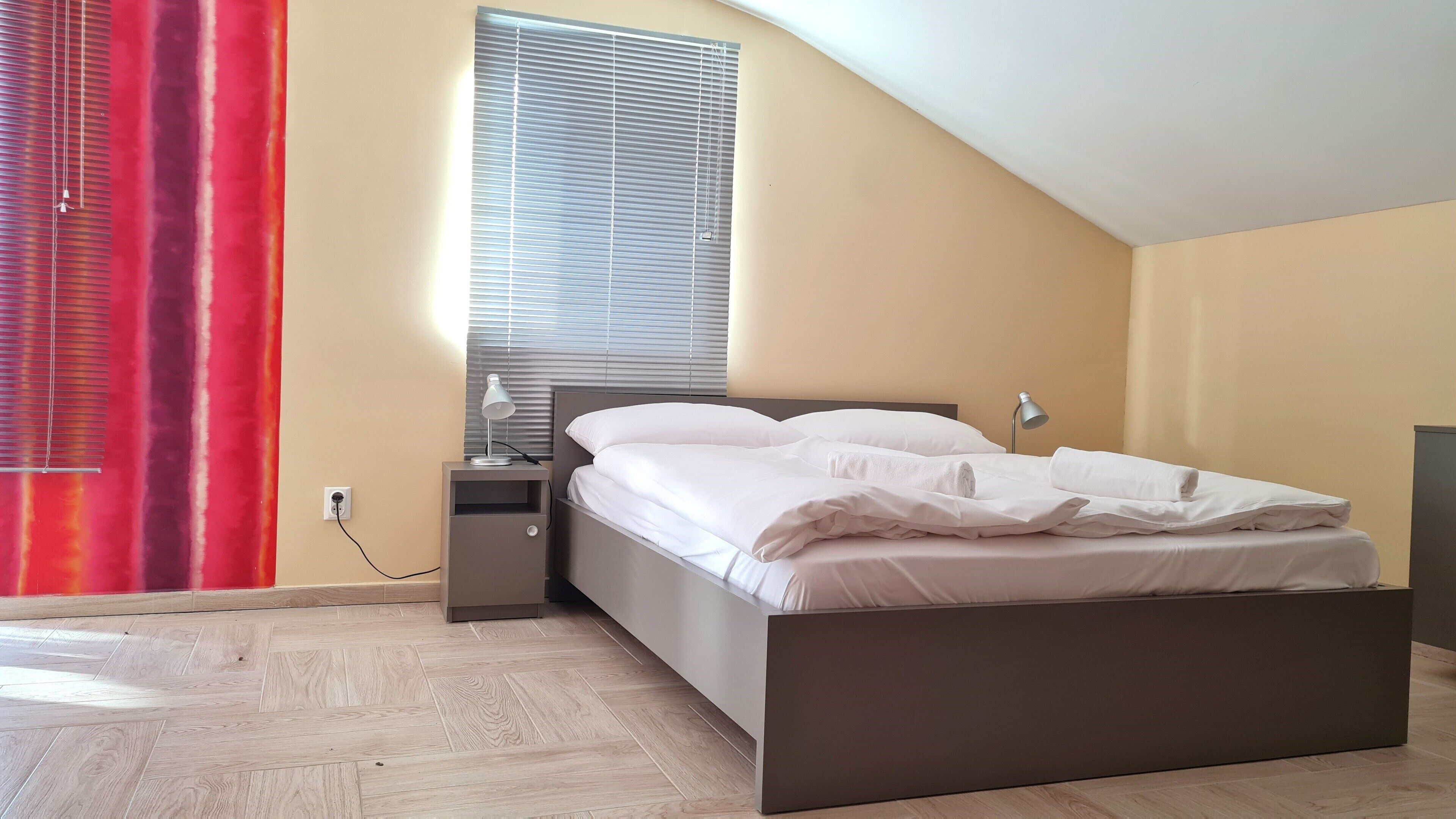 A bedroom with a bed, bedside table, lamp, and a window with blinds.