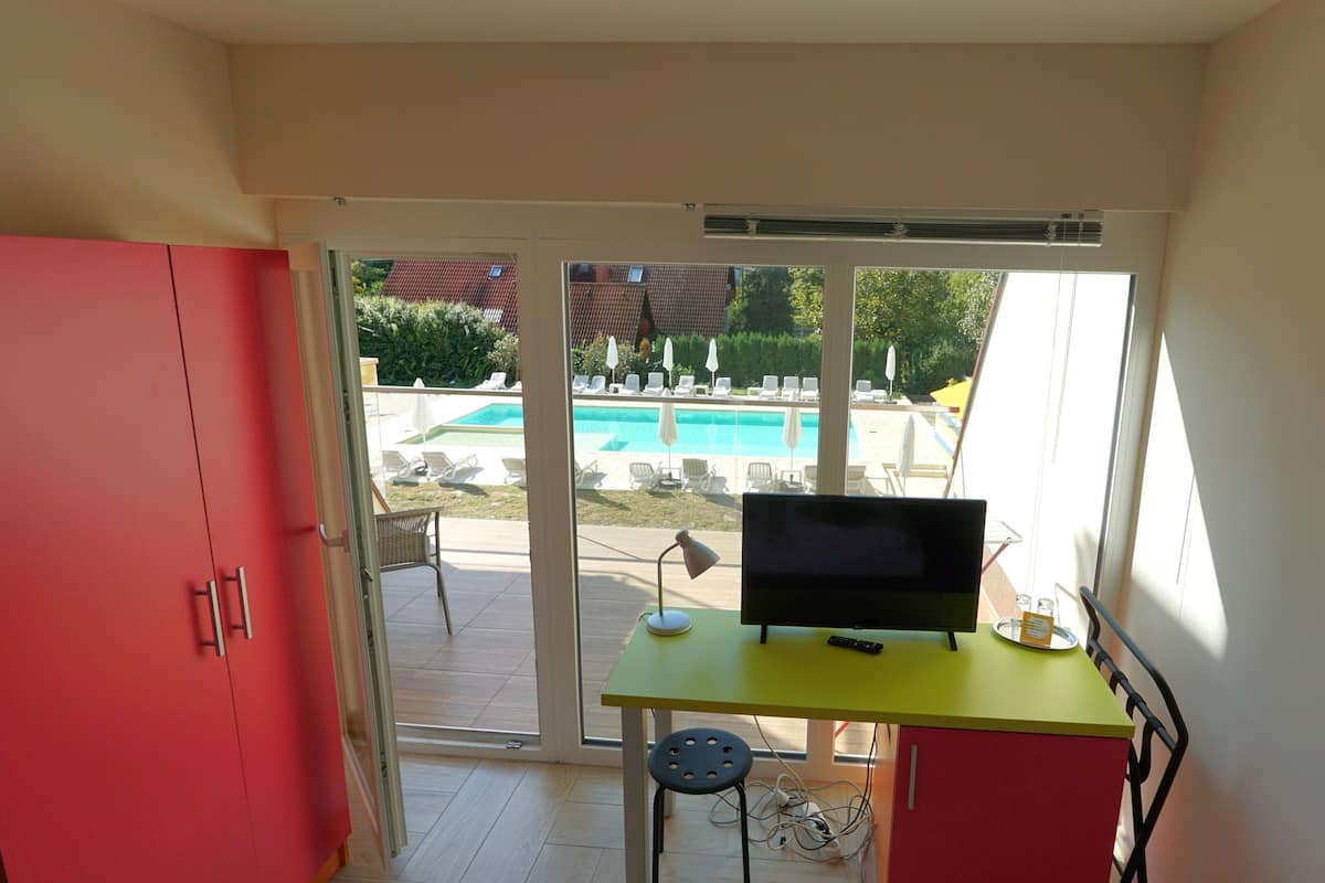 A room with a TV on a desk, a red cabinet, and a view of a swimming pool outside.