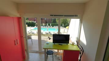 A room with a TV on a desk, a red cabinet, and a view of a swimming pool outside.