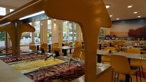 A buffet area with various food options, including meats and cheeses, in a well-lit indoor setting with yellow chairs and tables.