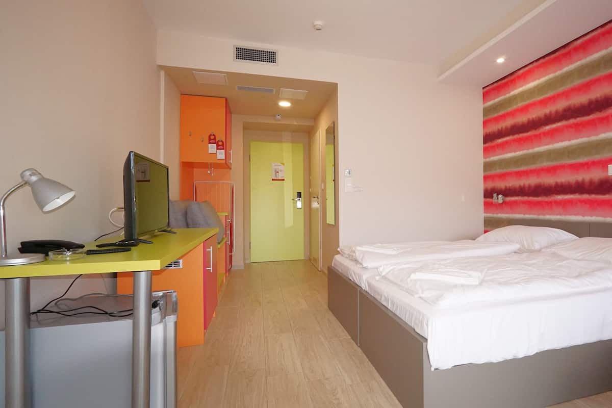 A hotel room with a bed, a desk with a computer, a chair, and a bathroom visible through an open door.
