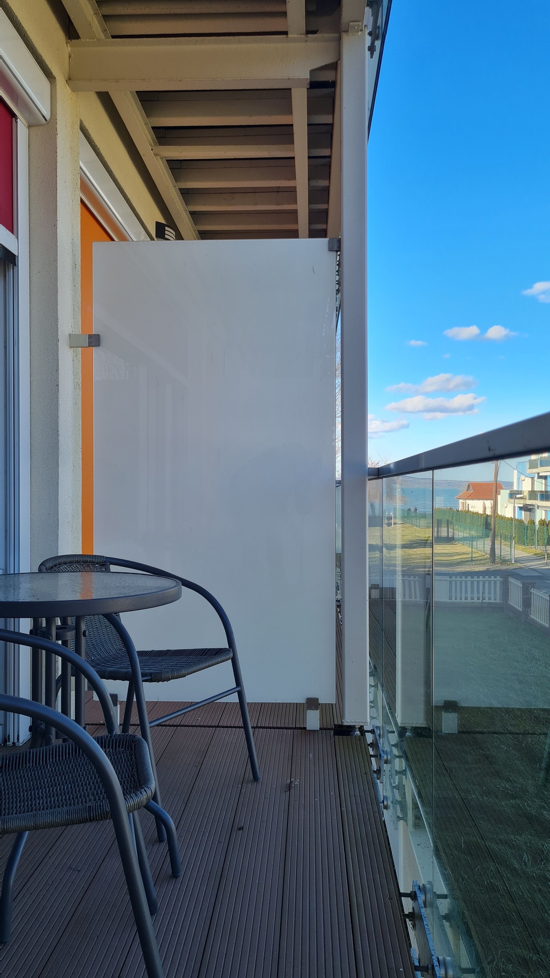 Un balcón con una mesa y sillas, un separador blanco y vistas de un edificio y el paisaje.