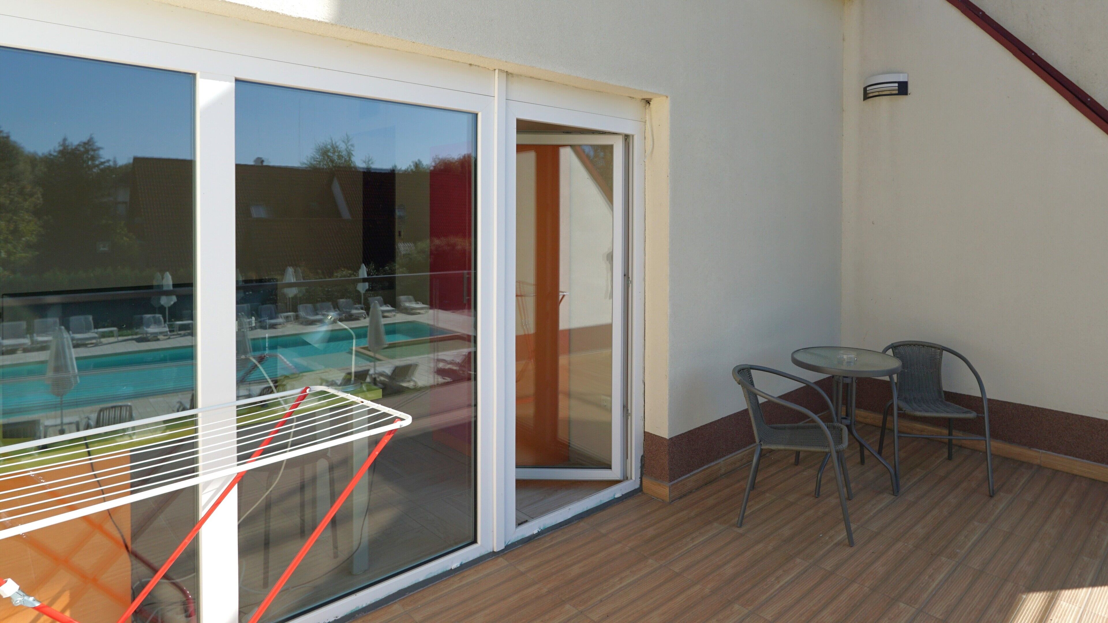 Un balcón con puerta de vidrio que da a una zona de piscina, una mesa pequeña y dos sillas.
