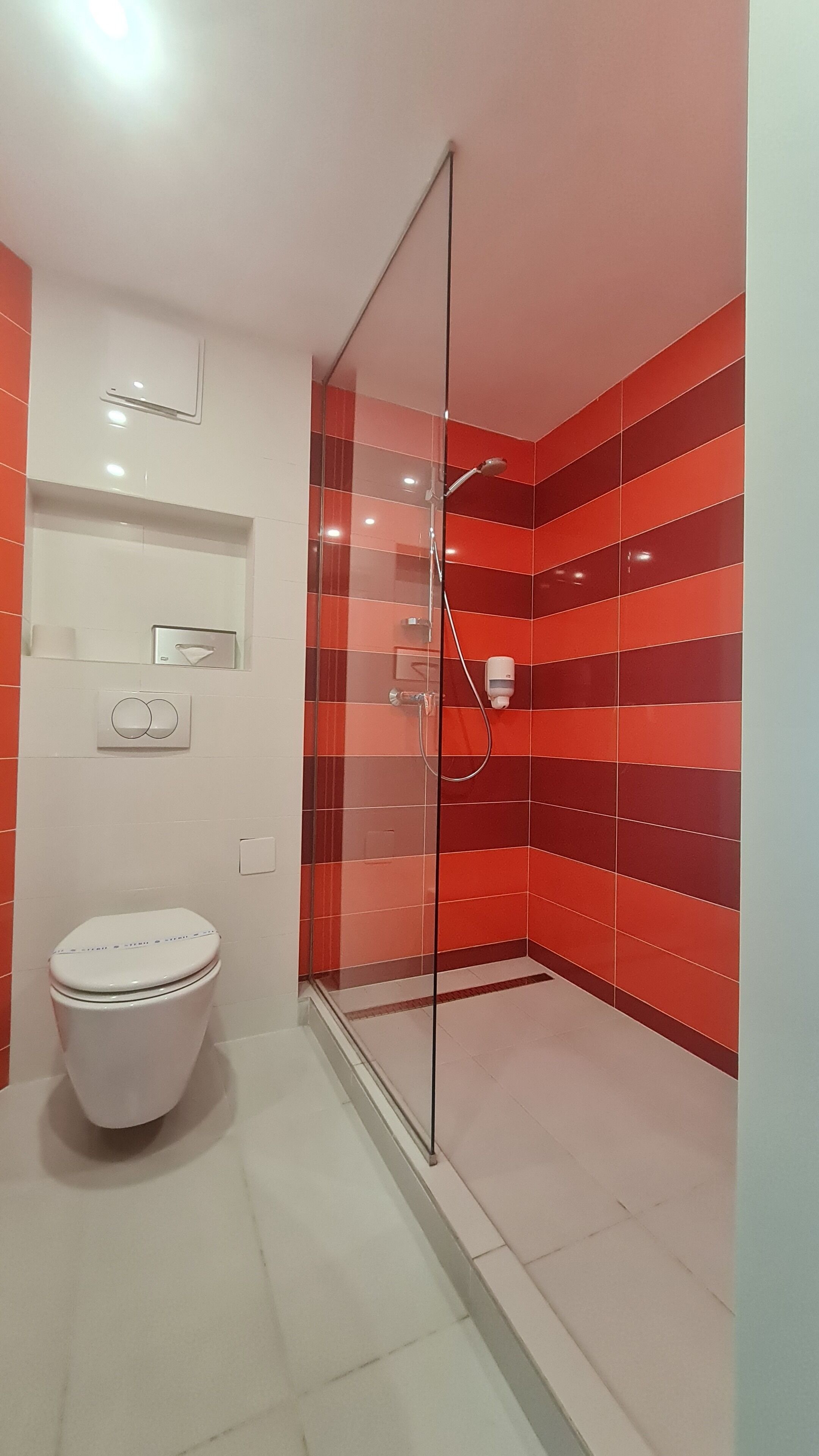A modern bathroom with a glass-enclosed shower, a toilet, and a hand dryer.