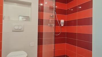 A modern bathroom with a glass-enclosed shower, a toilet, and a hand dryer.