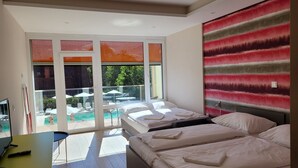 A modern hotel room with a bed, a desk, and a view of an outdoor pool area.