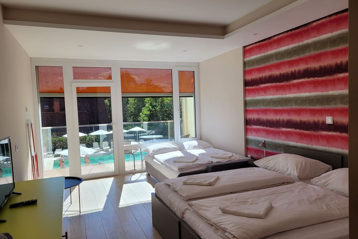 A modern hotel room with a bed, a desk, and a view of an outdoor pool area.