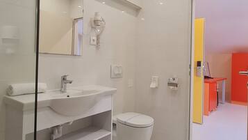 A modern bathroom with a white sink, mirror, and toilet. There is a glass partition on the left, and a red door in the background.