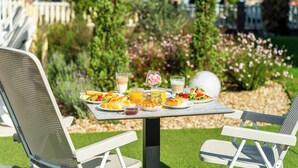 An outdoor dining table with chairs, surrounded by a garden with various plants and flowers.