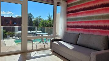 A modern living room with a sofa, a view of a pool, and a balcony with outdoor furniture.