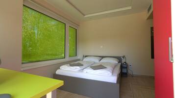 A bedroom with a bed, a window, a desk, and a red wall.
