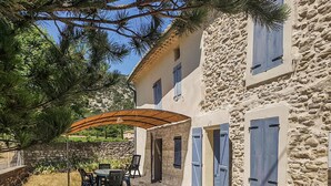 A stone building with a covered patio, outdoor seating, and blue shutters. - Cozy home in Malaucène (Malaucène)