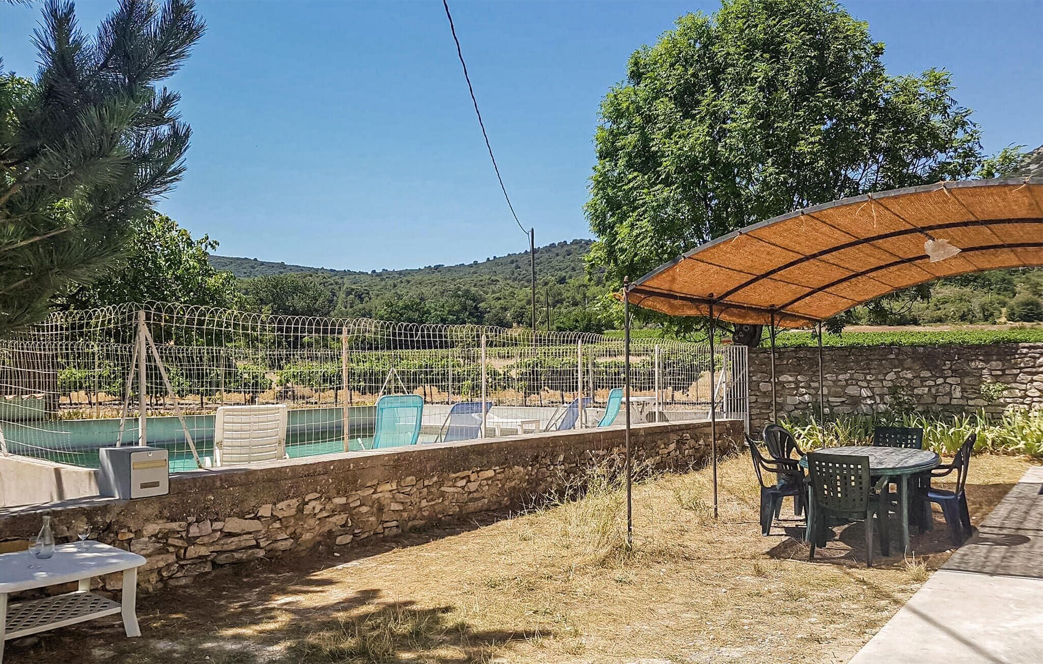A pool area with a stone wall, a covered seating area, and a view of a vineyard.
