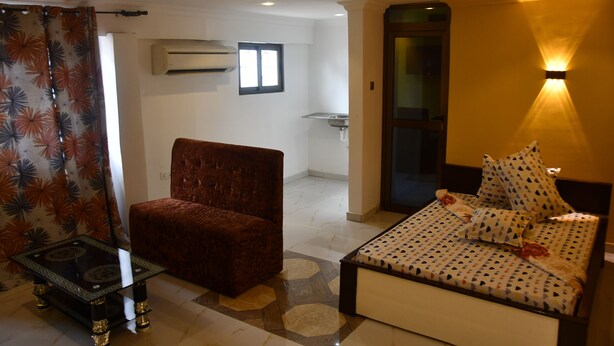 A bedroom with a bed, a chair, and a small table. There is an air conditioning unit on the wall and a window.