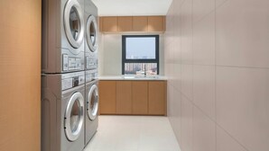 A compact laundry room with stacked washers and dryers, a window, and a sink. - Fairfield by Marriott Hangzhou Binjiang Puyan (Hangzhou)