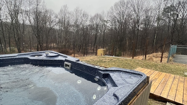 Ein Whirlpool mit einer Holzterrasse in einem von Bäumen umgebenen Garten.