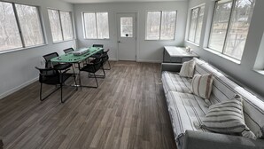 Ein geräumiger Raum mit großem Tisch und Stühlen, einem Sofa und zahlreichen Fenstern, die für natürliches Licht sorgen.