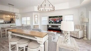 Un salón amplio con televisor grande, chimenea y comedor con taburetes.