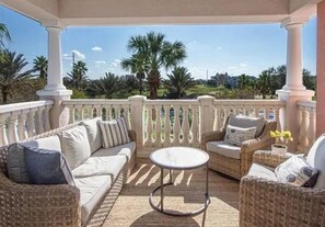 Relax in a serene outdoor space with a sofa, armchairs, and a small table amidst palm trees and city views.