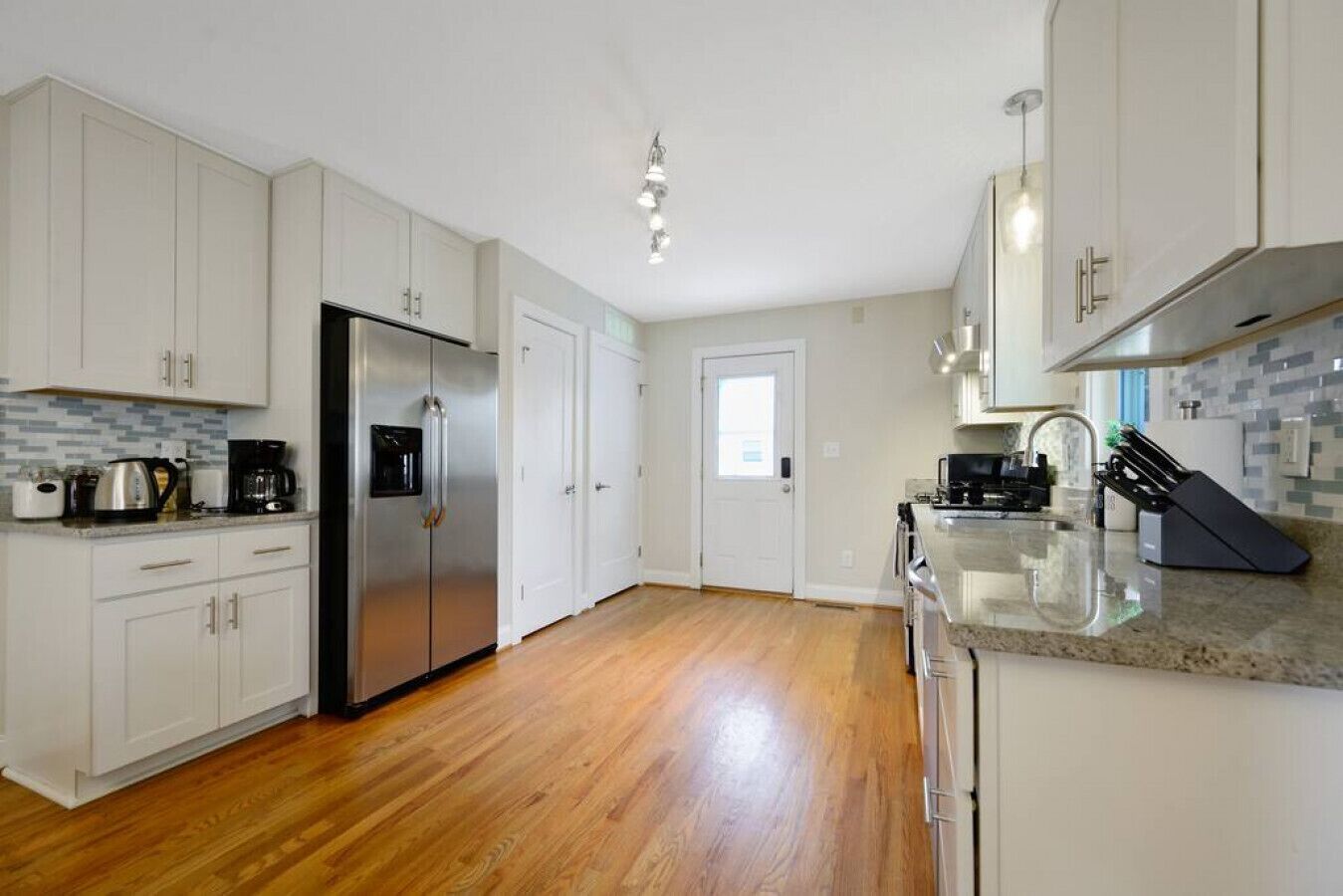 Una cocina moderna con armarios blancos, un refrigerador de acero inoxidable, una cafetera y un bloque de cuchillos.