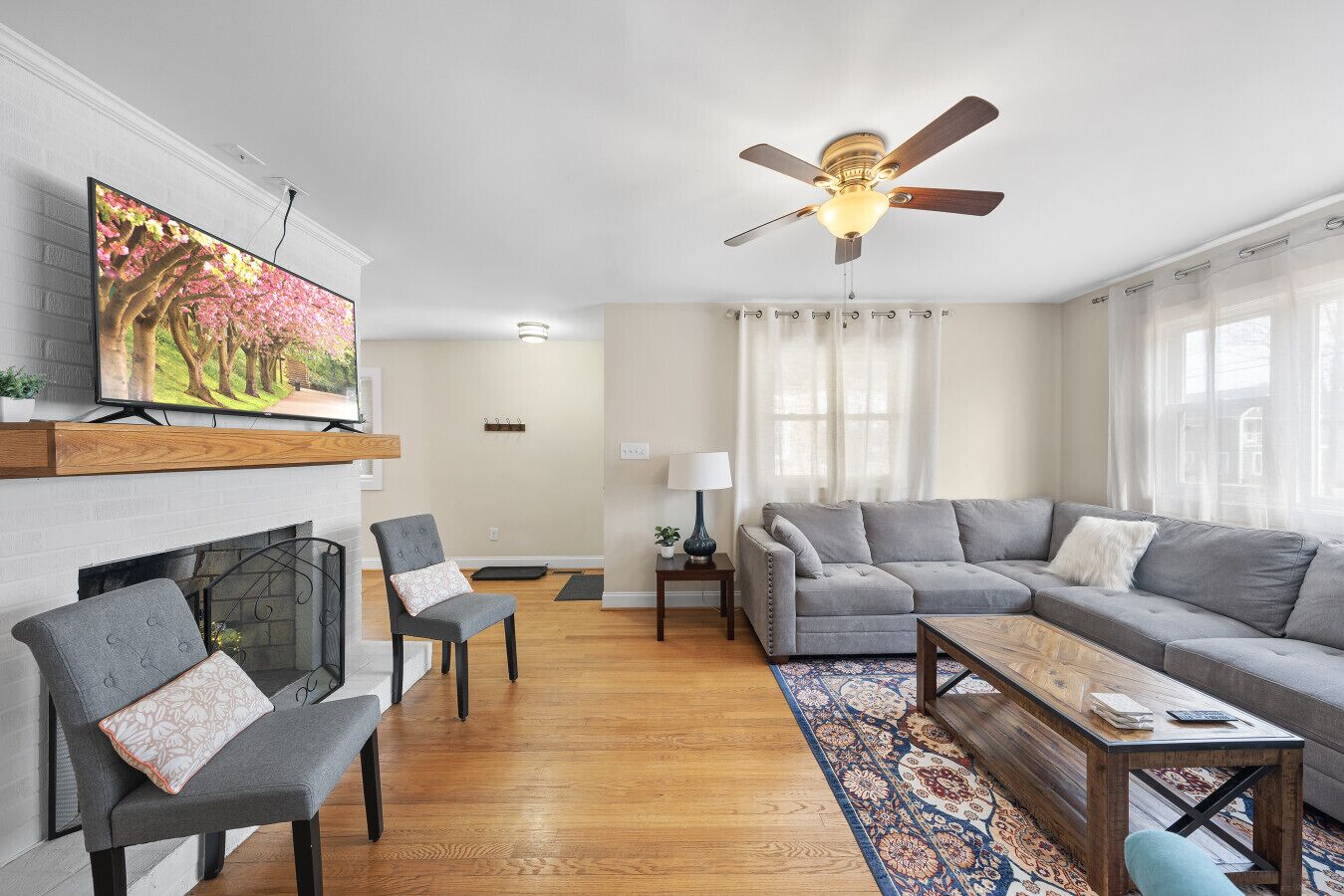 A living room with a fireplace, a grey sofa, a grey armchair, a coffee table, and a TV mounted on the wall.