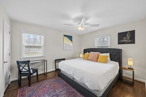 Ein Schlafzimmer mit einem Bett, einem Schreibtisch, einem Sessel, einem Deckenventilator und Kunstwerken an den Wänden.