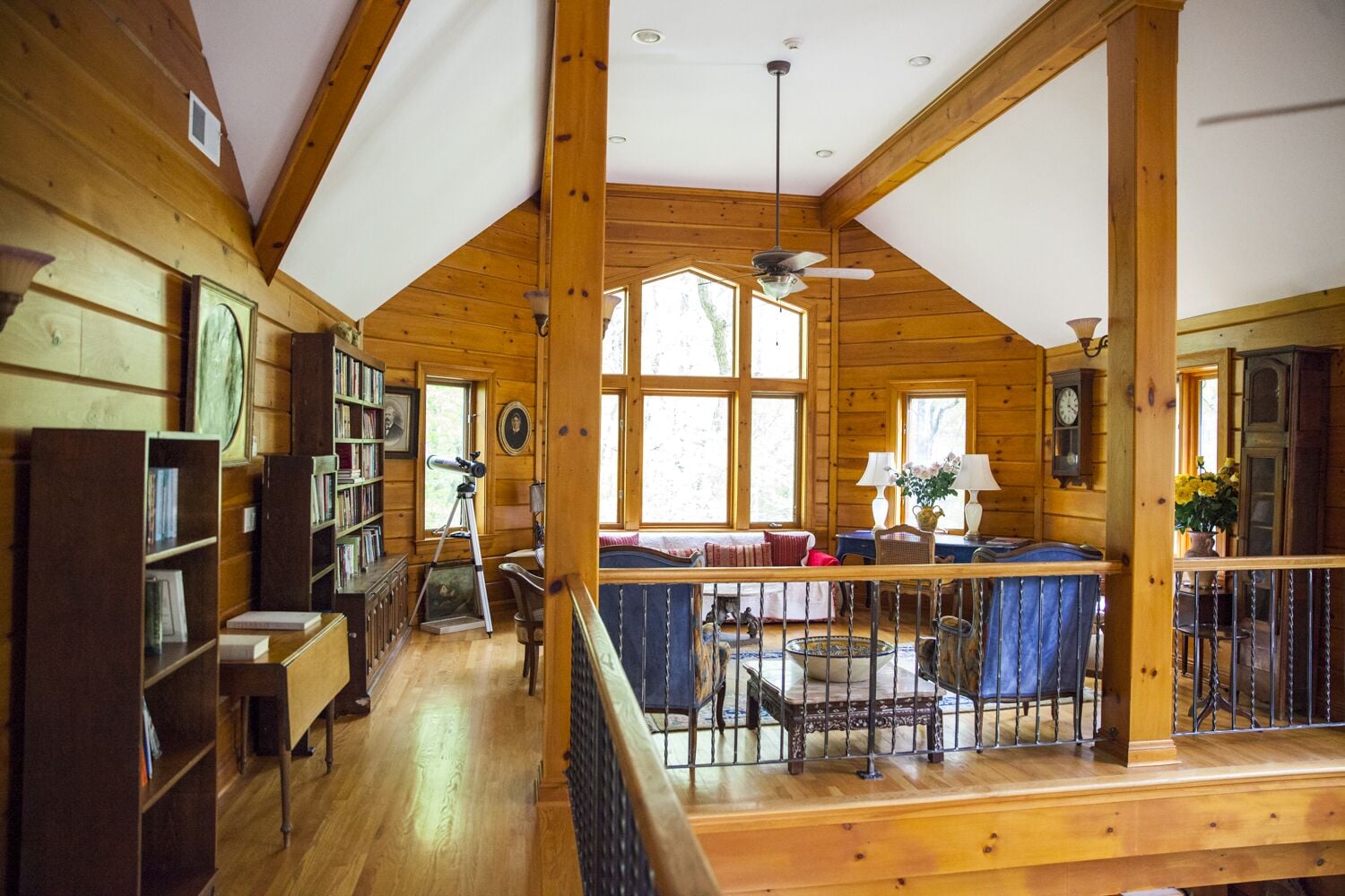 A spacious cabin with a high ceiling, wooden beams, a library, a dining area, and large windows.